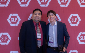Two men smiling in front of a red backdrop.